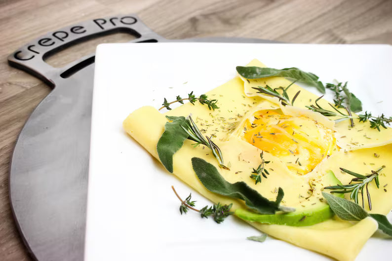 Savory brunch crepe topped with fried eggs and herbs on a carbon steel pan