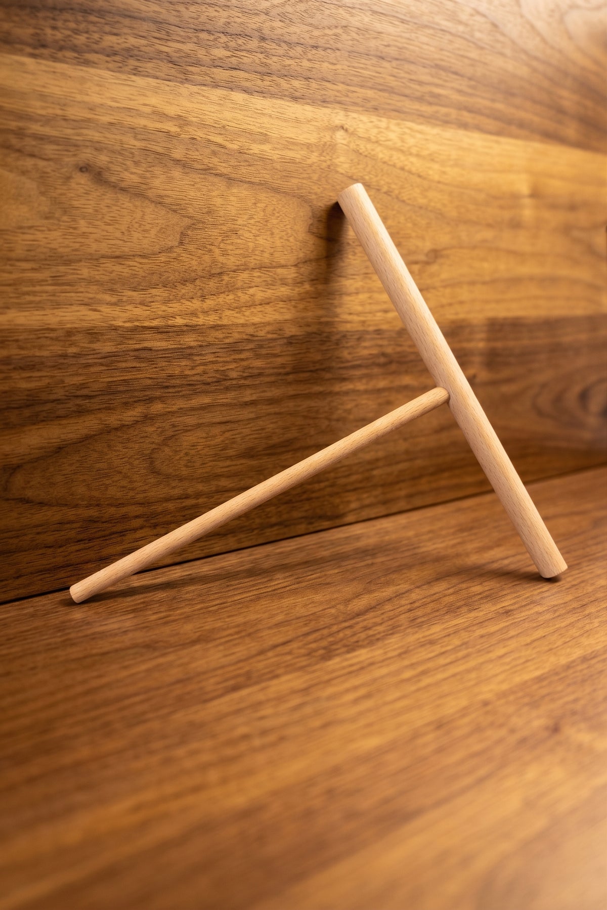 A minimalist wooden 7" crepe spreader T-shaped desk stand made of light natural wood, shown on a matching wood-grain surface with a warm, golden-brown background.